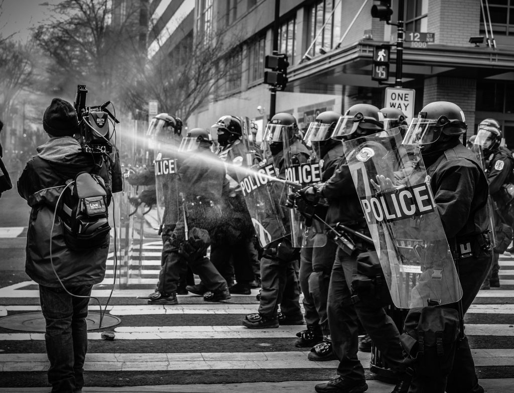 b&w photo of line of police with a fire hose aimed at a camera person